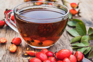 Cup of rosehip tea with fresh berries on a wooden table.