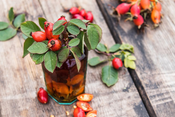 Tincture in a glass bottle with red rosehip berries on a wooden table.