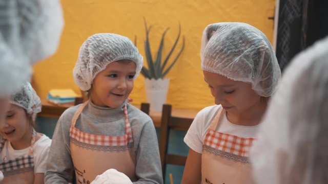 Children in disposable cap and apron making dough on cooking lesson in culinary school. Happy children preparing dough for baking pie. Cooking master class in bakery