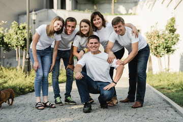 Happy family in white T-shirt and jeans emracing and having fun. Parents with their adult children walking in the park. Family time concept