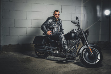 Plakat Brutal bearded biker in leather suit is sitting on his bike while holding a helmet.