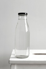 glass bottle with clear water on a wooden chair on a white wall background