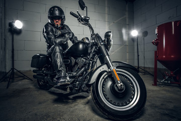 In dark garage bearded biker on motorbike is posing for photographer on his bike.
