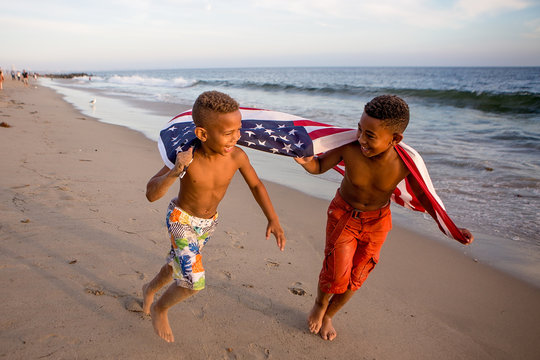 Patriotic fun at the beach boys running with the American flag - Powered by Adobe