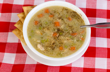 Overhead View of Bowl of Chicken Soup with Saltine Crackers on Red Plaid BG