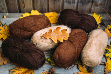   Skeins of wool for knitting decorated with autumn leaves on a wooden background.
