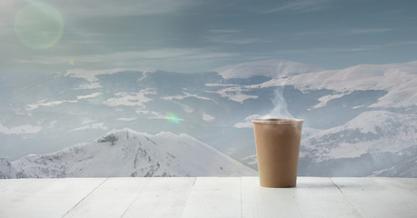 Single tea or coffee mug and landscape of mountains on background. Cup of hot drink with snowly look and cloudly sky in front of it. Warm in winter day, holidays, travel, New Year and Christmas time.