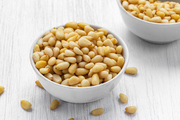 Pine nuts lie in two white bowls on a white wooden surface, side view from above