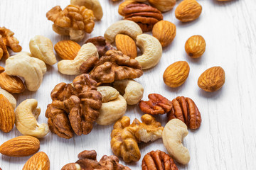 Assorted nuts scattered on a white wooden surface, side view from above