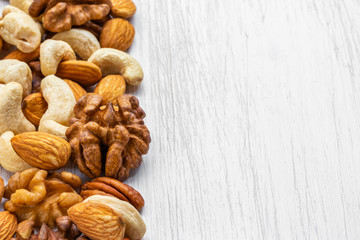 Walnuts, cashews, almonds and pecans lie on the left on a white wooden surface, on the right is an empty place, side view from above
