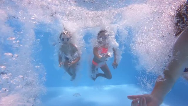 Underwater view of having fun group of children jumping and diving into swimming pool at pool party in summer sunny day. Happy children. Slow motion. Childhood, friendship, vacation concept