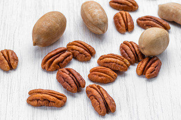 Pecans peeled and in shell lying on a white wooden surface, side view from above