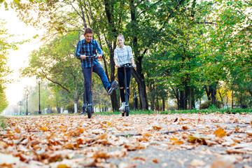 Cute teenager girl and boy riding electric kick scooter in the park.