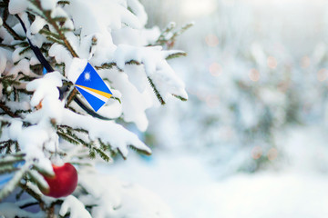 Christmas Marshall Islands. Xmas tree covered with snow, decorations and a flag of Marshall Islands. Snowy forest background in winter. Christmas greeting card.