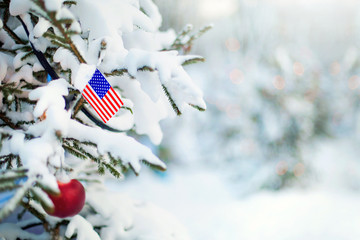 Christmas United States. Xmas tree covered with snow, decorations and a flag of USA. Snowy forest background in winter. Christmas greeting card. - 299398742
