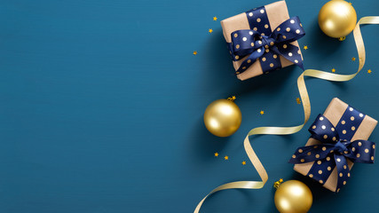 Flat lay Christmas gift boxes, golden balls, confetti, ribbon over blue background. Xmas banner...