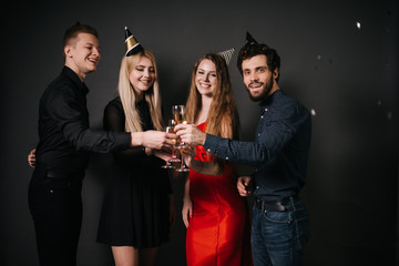Two attractive guys and two beautiful girls clinking with champagne glasses and celebrating new year. Shooting in professional studio on isolated black background.