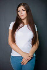  Young, beautiful girl in a white T-shirt and blue jeans. Studio photo on a gray background.