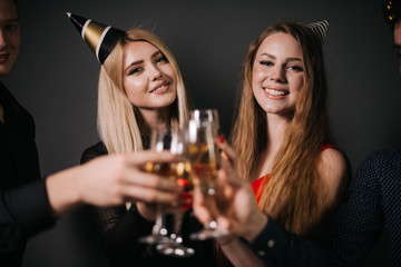 Close-up of man and woman clinking with champagne glasses. Four beautiful and cheerful friends in festive clothes on background.