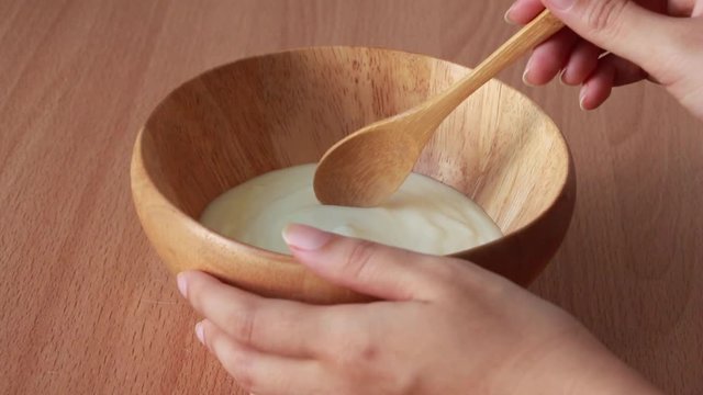 woman eating organic yogurt with spoon from wood bowl