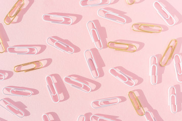 Pink and golden paper clips on a pastel pink background. The concept of stationery, study, office, business. Minimalism, hard shadows, pattern.