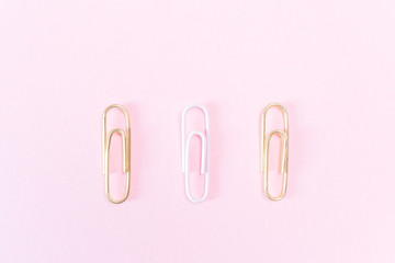 Pink and golden paper clips on a pastel pink background. The concept of stationery, study, office, business. Minimalism.