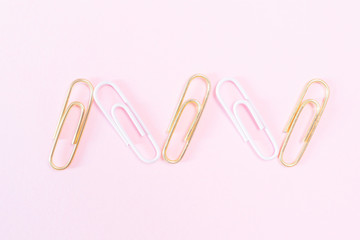 Pink and golden paper clips on a pastel pink background. The concept of stationery, study, office, business. Minimalism.