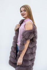 Beautiful young woman in fur coat on white wall. Beauty and fashion.