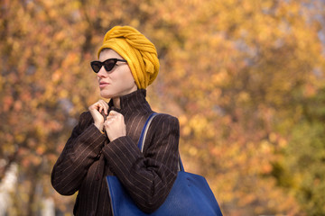 Portrait of a stylish woman  in sunglasess and scarf on head walking in autumn scenery