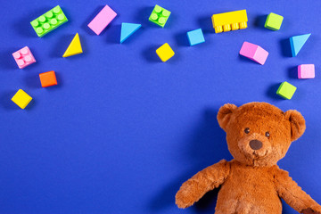 Baby kids toys frame with teddy bear and colorful wooden blocks and cubes on blue background. Top view