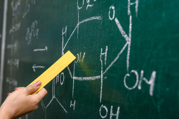 Female hand pointing at chemical formula on blackboard close up