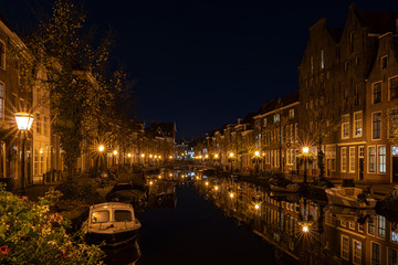 A night shot from the old bridge (The Kerkbrug) on the Oude Rijn with numerous boats and illuminated old canal-side houses, Leiden, the Netherlands
