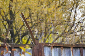 barbed wire on rusty fence on the background of yellow autumn trees. protection of territory, protection of property, two methods of protection