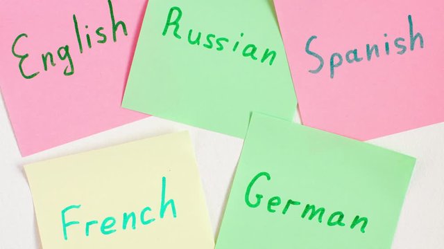 Stop motion animation top view flat lay of five languages english, german, russian, spanish and french which written on the reminder notepaper of different colors       