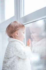 little girl in a winter coat looks out the window