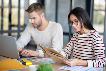 Wife in glasses looking at post mail while sitting near husband