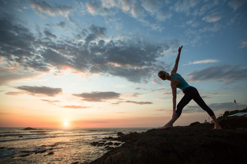 Yoga female sees off the sun on the ocean coast. Exercises.
