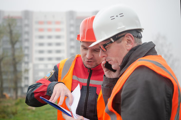 Obraz premium An engineer with a hard hat and helmet discussing a project at a construction site with a team leader in autumn or winter. architecture construction concept. Industrial safety