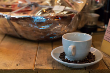 An empty white coffee cup in a bowl with brown beans stands on a wooden table