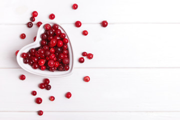 Fresh cranberry berries in a heart shaped bowl on white wooden table