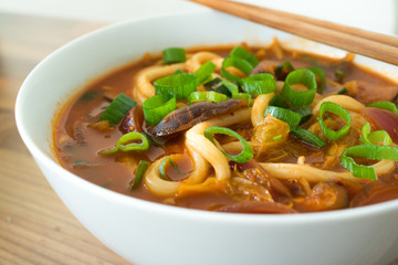 Food photography of a spicy Korean Asian noodle soup in a white bowl.