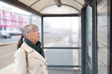 Senior woman looking at timetable at bus stop