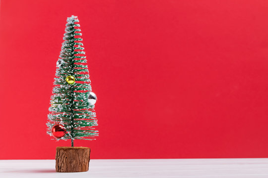 Small artificial Christmas tree decorated with balls and snow on the red background