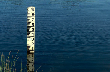 Close up of an old depth marker post with reflection on the rippling blue surface of an open pond....