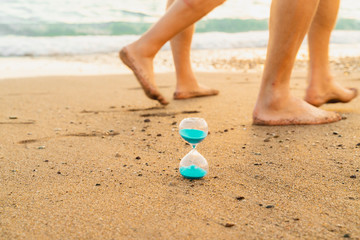 Time is running fast. Hourglass on the wet sea sand and traces of leaving legs symbolize the transience of time, everything passes. Will we leave our mark in life?