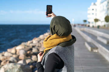 woman with headscarf taking selfie by ocean 