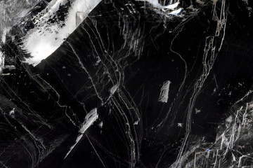 Thin layer of broken ice against black. Textured abstract background with reflections.