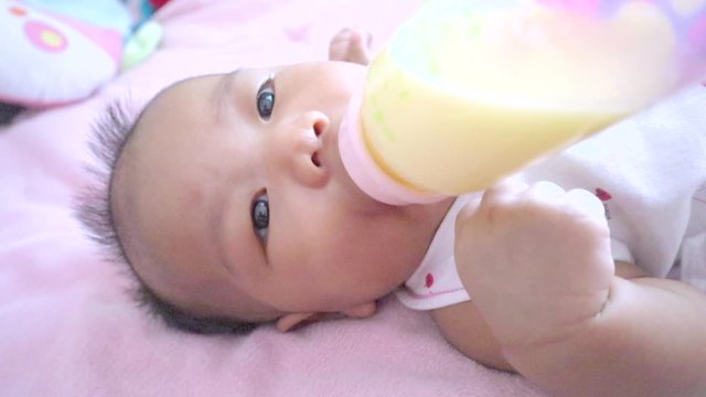 Newborn baby is sucking mother's milk, which has been pumped into a bottle from a breast pump. 3-month-old Asian male baby Sucking deliciously on the bed.