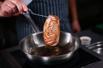 A chef fries a piece of duck. Cooking in the kitchen in a restaurant. Photo without a face. Healthy eating concept.