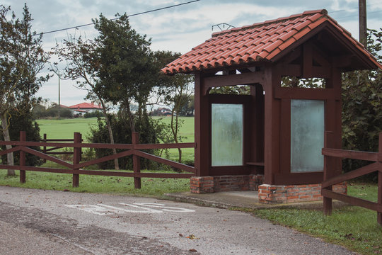 Wooden bus station in the village. Empty rural bus station along road with fence and trees. Travel and destination concept. Transportation concept. Countryside voyage. Journey background. 
